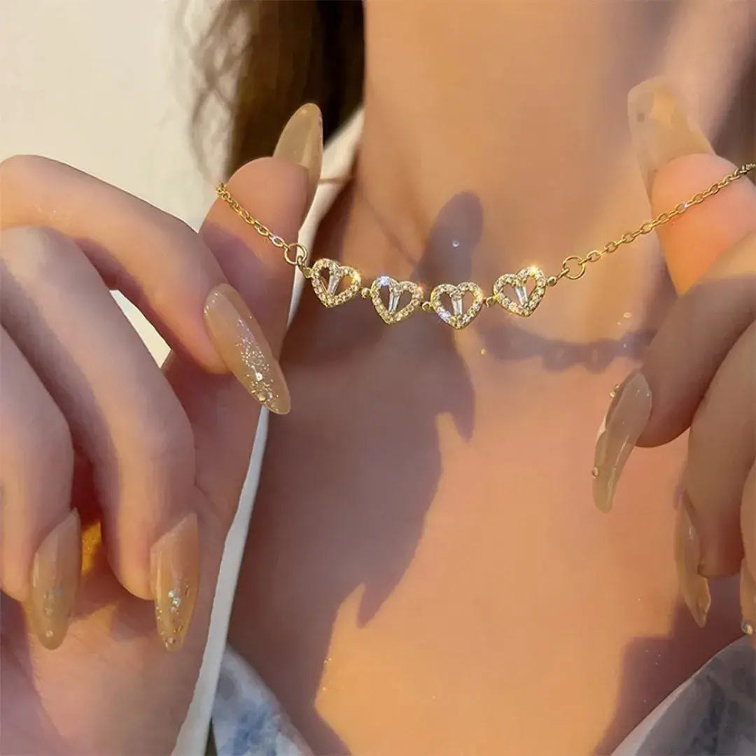 Colar Romantizze dourado com pingente de corações e zircônia em destaque no colo da modelo com iluminação quente.