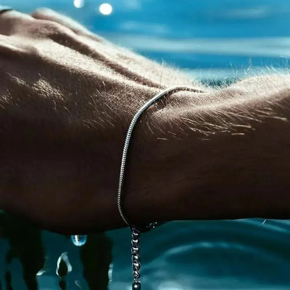 Pulseira prata em aço inoxidável estilo corrente cobra usada no pulso masculino, com fundo de piscina – Romantizze