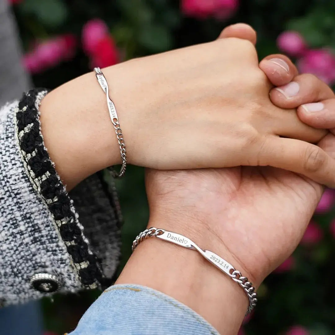 Casal com pulseiras Mobius prateadas Romantizze, exibindo conexão e personalização com nomes gravados.